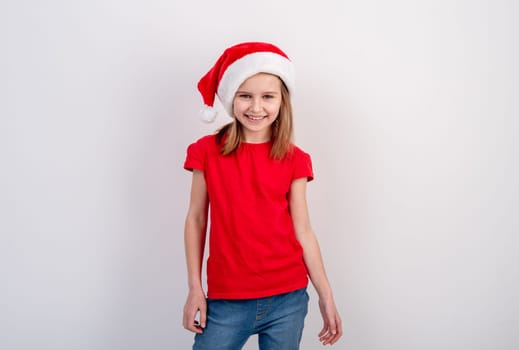 Little Girl In Red T-Shirt And Santa Hat Poses For A Festive Photo On A White Background