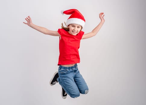 Little Girl In Red T-Shirt And Santa Hat Is Jumping In A Festive Photo On A White Background