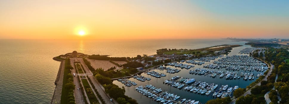Aerial view of bustling Burnham Harbor in Chicago, capturing the serene glow of sunrise over the vibrant marina and city skyline