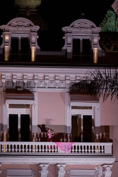 Monaco, Monte-Carlo, 12 November 2022: A girl plays the violin on the balcony of the famous Casino Monte-Carlo is at night, pink dress, attraction night illumination. High quality photo