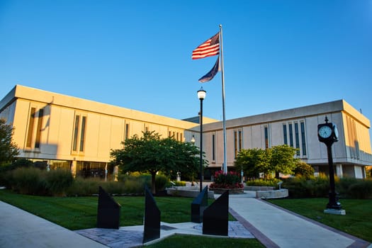 Golden hour sunrise over Delaware County Court, Indiana, showcasing patriotism with a prominent American flag, modern architecture, and tranquil garden.
