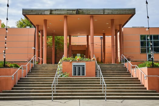 Modern Art Center Entrance in Indianapolis, Indiana 2023 - A tranquil daytime scene featuring a contemporary terracotta-hued building with concrete steps, metal railings, and a floral-adorned plaque.