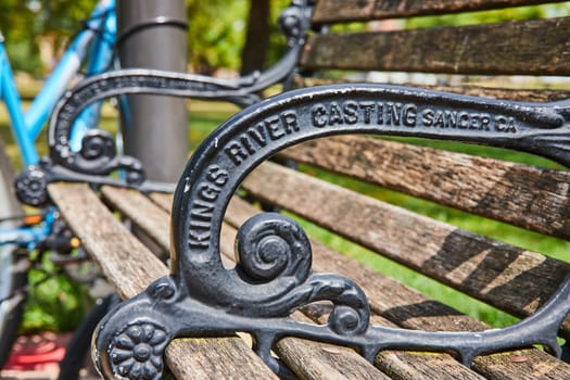 Vintage Kings River Casting park bench with weathered wood slats and intricate armrest in Indianapolis park, with bright blue bicycle in background, 2023.