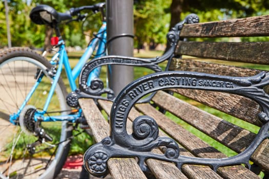 Vintage park bench with Kings River inscription in an urban Indianapolis setting, featuring a bright blue bicycle against a serene green backdrop, 2023
