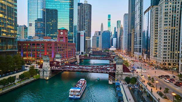 Image of Chicago boat going under canal bridge aerial with city lights and skyscrapers at blue hour, tourism
