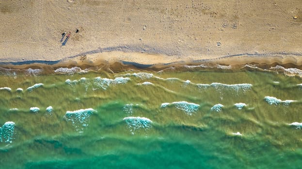 Image of Aerial above green water waves on sunny day with beach along coast with tourists traveling on sand