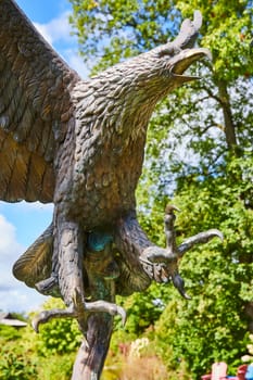 Bronze eagle sculpture majestically posed against green foliage under natural light, in Elkhart's Botanic Gardens, Indiana, 2023