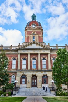 Image of Elkhart County courthouse front steps leading to entrance on blue sky day with fluffy white clouds