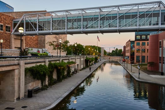 Modern pedestrian bridge reflecting on the tranquil canal at blue hour, downtown Indianapolis 2023, symbolizing urban development and serene city living.