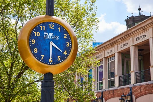 Indiana Historical Society's golden-rimmed public clock in urban Indianapolis, displaying time and heritage under a vibrant summer sky.