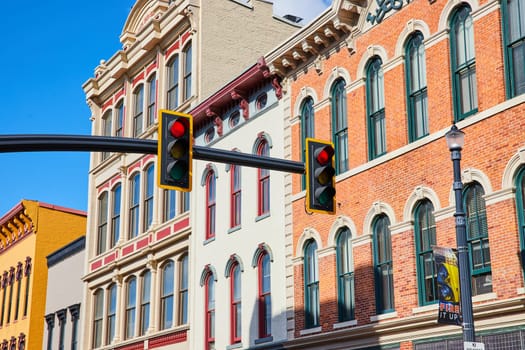 Vibrant urban scene in Downtown Muncie, Indiana, showcasing historic red and yellow brick buildings against a clear blue sky, with modern traffic signals and local cultural elements.