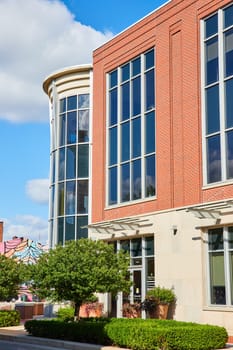 Modern glass and brick building under blue sky in Downtown Muncie, Indiana, 2023, showcasing urban development and architectural design with well-maintained landscaping.
