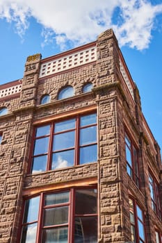 Sunlit view of an impressive sandstone building with detailed stonework and large windows, exhibiting classic architecture in Downtown Muncie, Indiana, 2023