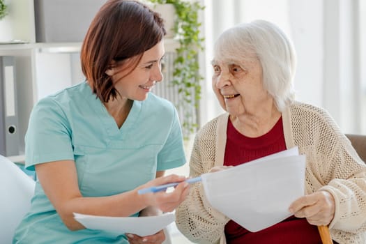 Smiling Nurse Gives Elderly Woman Documents To Read In Doctor'S Office