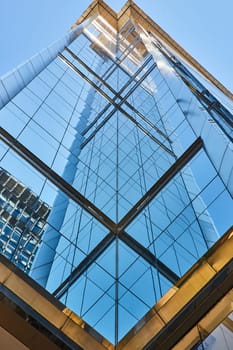 Image of Middle upward view of blue windows of tall skyscraper creating mirror image on summer day