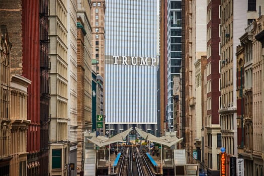 Daytime scene of Trump Tower, a modern skyscraper, contrasting with traditional architecture in bustling downtown Chicago, Illinois, as trains bustle along elevated tracks, 2023.