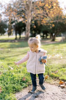 Little girl with a plush cat in her hand walks through the autumn park looking at the fallen leaves. High quality photo
