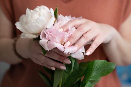 female hands with a beautiful peach manicure design, color 2024, pastel colors, delicate spring dewy peonies in the hands of a model, high quality photo