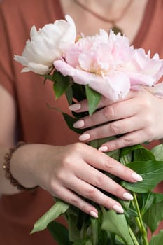 female hands with a beautiful peach manicure design, color 2024, pastel colors, delicate spring dewy peonies in the hands of a model, high quality photo