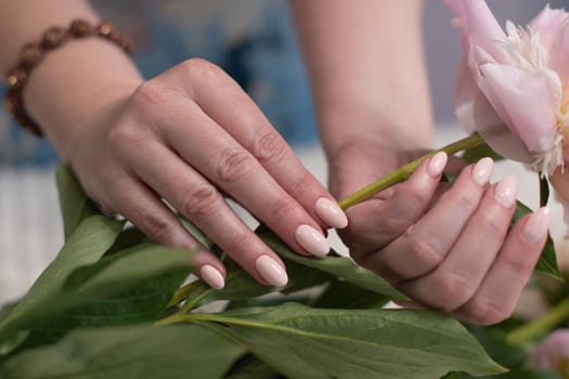 female hands with a beautiful peach manicure design, color 2024, pastel colors, delicate spring dewy peonies in the hands of a model, high quality photo