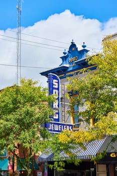 Image of Retro sign on shop behind lush green trees in summer with blue sky and puffy white cloud, Indiana