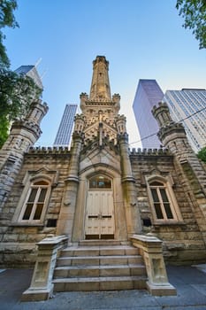 Image of Chicago Water Tower front with lit tower and bright skyscrapers behind framed by lush green trees