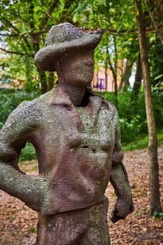 Textured human figure sculpture amidst serene woodland at the Art Center, Indianapolis, epitomizing tranquility with its weathered wooden texture and confident posture.