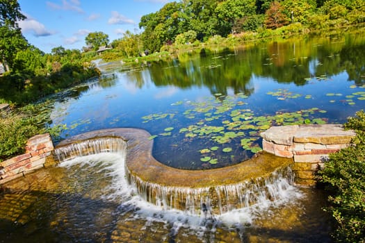 Vibrant daytime scene of serene waterfall in Elkhart Botanic Gardens, Indiana, 2023, with lush greenery and tranquil lily pad pond