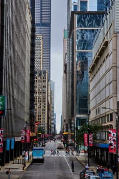Image of Tourists and pedestrians on Chicago street corridor between skyscraper buildings on gloomy day