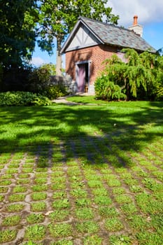Charming historic brick cottage with purple door nestled in sunlit Botanic Gardens, Elkhart, Indiana, offering a serene retreat