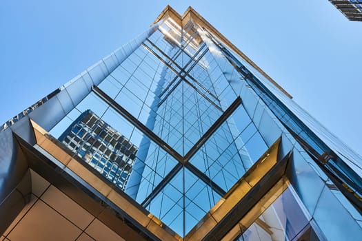 Image of Middle upward view of tall skyscraper corners creating mirror image on blue windows in summer