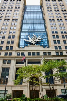 Image of Chicago public art, abstract flame sculpture on building with reflective blue windows and green tree