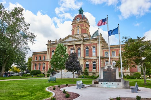 Image of Elkhart County courthouse under cloudy blue sky and memorial with flags, law and order, Indiana