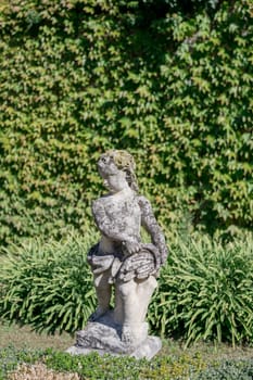 Antique sculpture of a little boy in a green garden. High quality photo