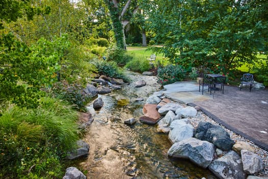 Tranquil 2023 Garden Scene in Elkhart, Indiana's Botanic Gardens, Featuring a Natural Stream, Lush Greenery, and Outdoor Patio