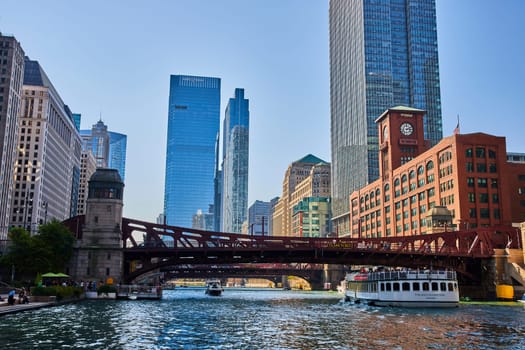 Image of Chicago canal with tour boats under red bridges with blue skyscrapers and office buildings, summer