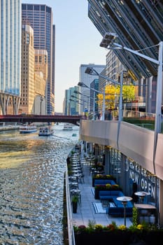 Image of Waterside patio on Chicago canal with tour boats passing under bridge with line of skyscrapers