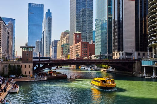 Image of Yellow tour boat on sunny Chicago canal with bridge and skyscrapers along waterway, USA tourism