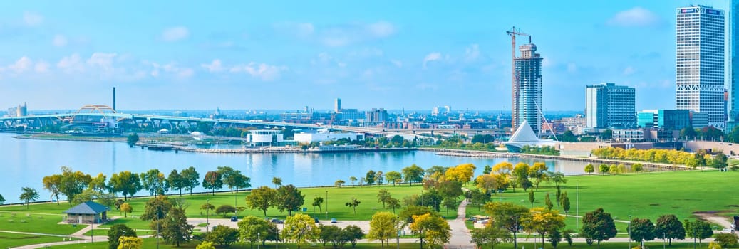 2023 aerial view of Milwaukee's skyline featuring under-construction skyscrapers, expansive green park, and tranquil Lake Michigan, captured by DJI Mavic 3 drone