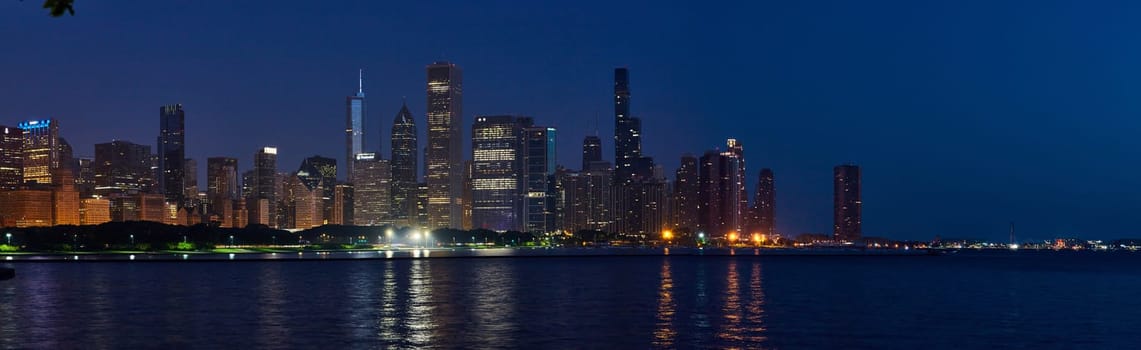 Panoramic twilight view of Chicago's illuminated skyline showcasing high-rise buildings reflecting on Lake Michigan, 2023
