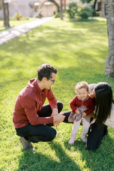 Mom tickles a little girl sitting next to dad in a sunny meadow. High quality photo