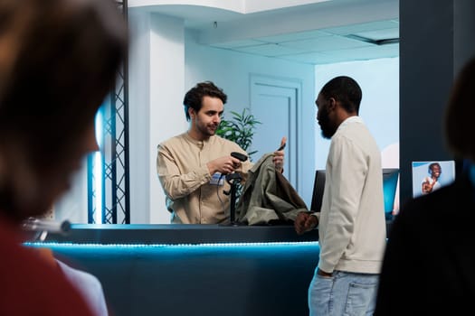 Cashier scanning apparel items for customer at clothing store counter. African american man talking with fashion boutique employee while buying shirt and waiting at cash register