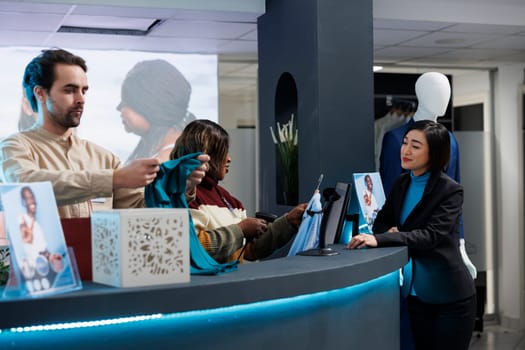 Fashion boutique smiling diverse employees scanning and packing clothes for client. Young asian woman making garment purchase at counter desk while shopping in fashion store