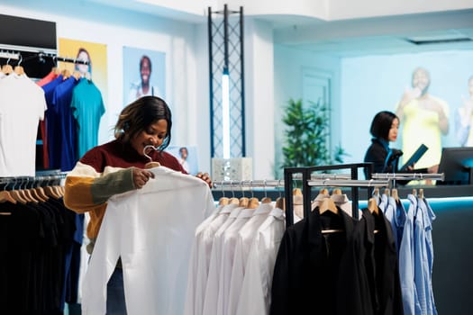 Smiling african american woman checking shirt fit and size while shopping in clothing store. Cheerful customer browsing apparel rack, selecting garment in womenswear mall department