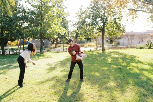 Smiling mom stands next to dad swinging a laughing little girl in his arms. High quality photo