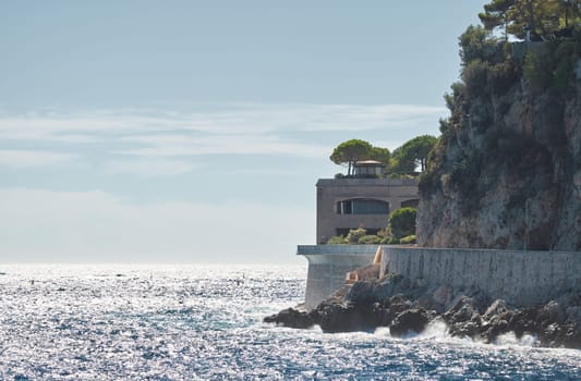 The rocky Promenade of Monaco on a clear sunny day, waves crashing on rocks, green trees on the mountain. High quality photo