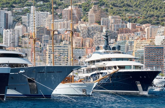 Few huge luxury yachts at the famous motorboat exhibition in the principality of Monaco, Monte Carlo, the most expensive boats for the richest people, mountain and residential complex on background. High quality photo