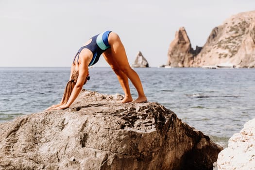 Yoga on the beach. A happy woman meditating in a yoga pose on the beach, surrounded by the ocean and rock mountains, promoting a healthy lifestyle outdoors in nature, and inspiring fitness concept