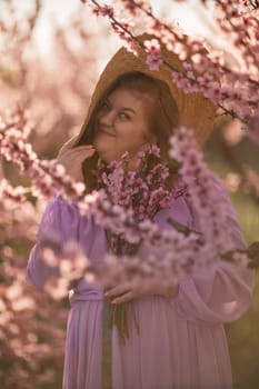 Woman blooming peach orchard. Against the backdrop of a picturesque peach orchard, a woman in a long pink dress and hat enjoys a peaceful walk in the park, surrounded by the beauty of nature