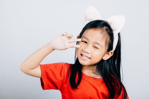 Portrait of a delighted Asian girl child wearing a red t-shirt beaming with a wide smile and sparkling eyes. Isolated joyful and innocent kid on a white background.
